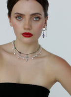 Woman wearing a black strapless top and multiple necklaces with a plain background
