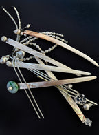 A set of traditional hair sticks made of mother-of-pearl, featuring iridescent white, beige, and green curved pieces, silver wire hairpins, and pearl bead strands, arranged on a solid black background.