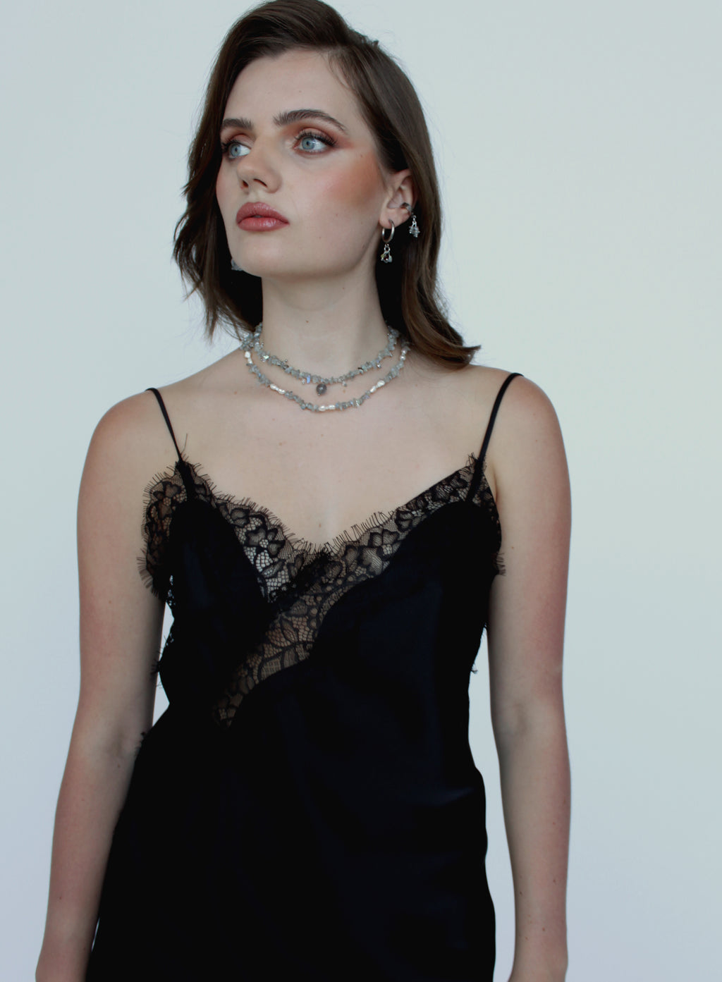 Woman wearing a black lace dress with a silver necklace against a plain background