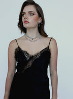Woman wearing a black lace dress with a silver necklace against a plain background