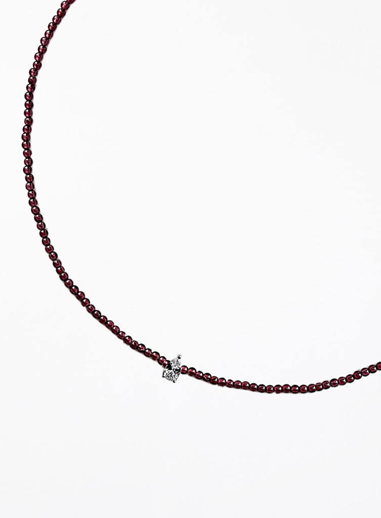 Thin garnet beaded necklace with tear drop charm on a white background
