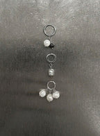 Three silver-toned ear cuffs with dangling pearl-like beads and a small black bead, arranged vertically on a dark gray textured surface.