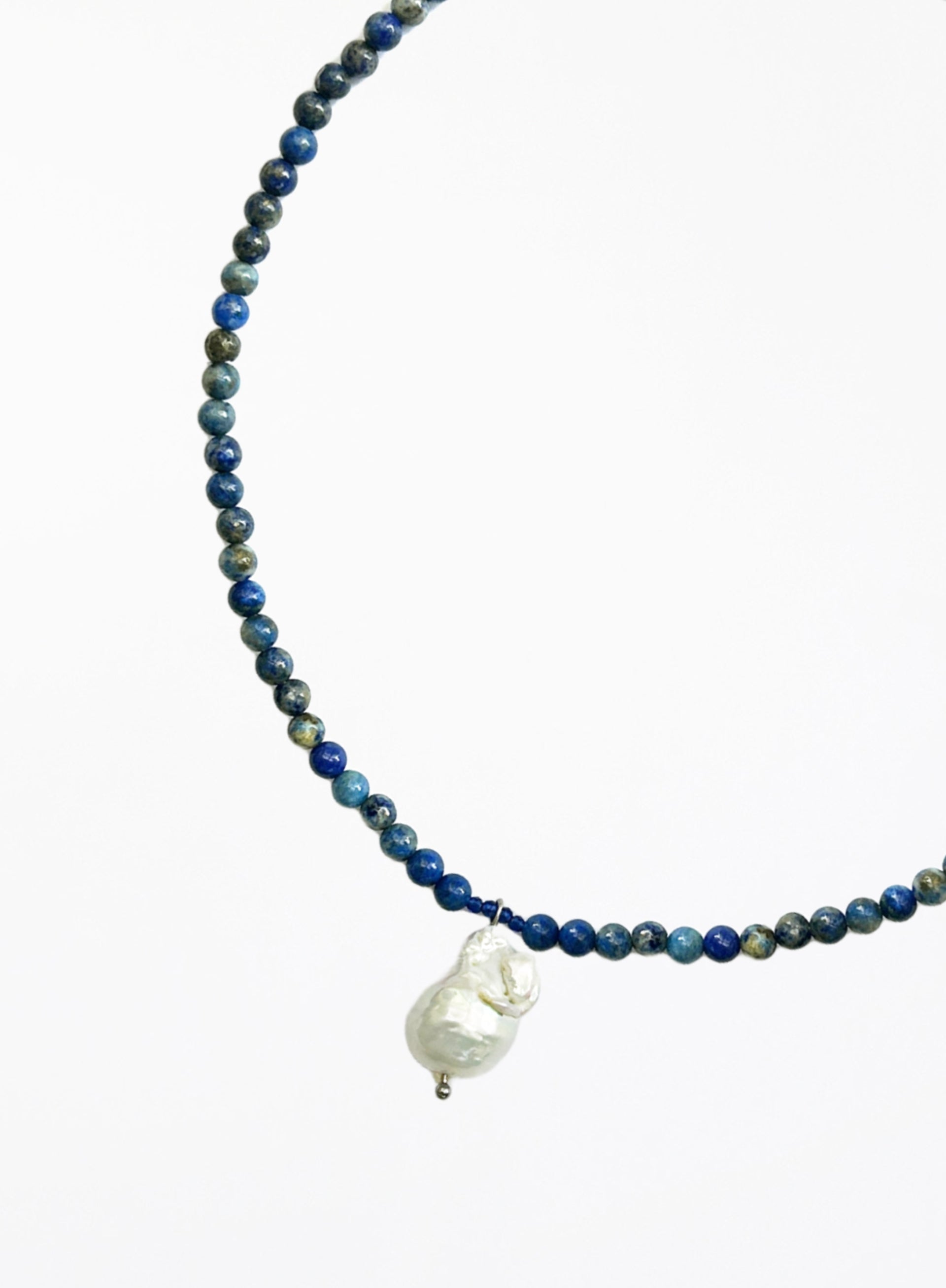 Necklace with blue beads and a white baroque pearl pendant on a white background