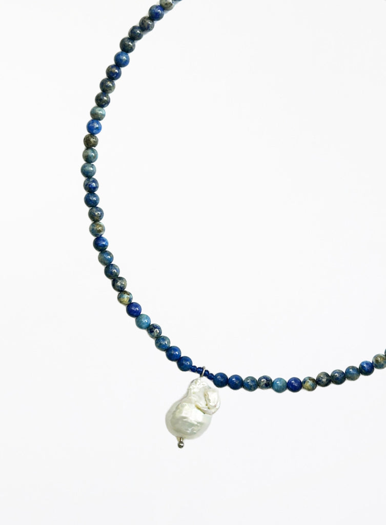 Necklace with blue beads and a white baroque pearl pendant on a white background
