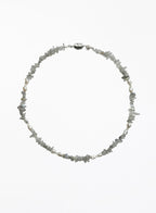 A delicate necklace made of small, irregular gray stone chips and white pearl beads, arranged in a circle on a plain white background.
