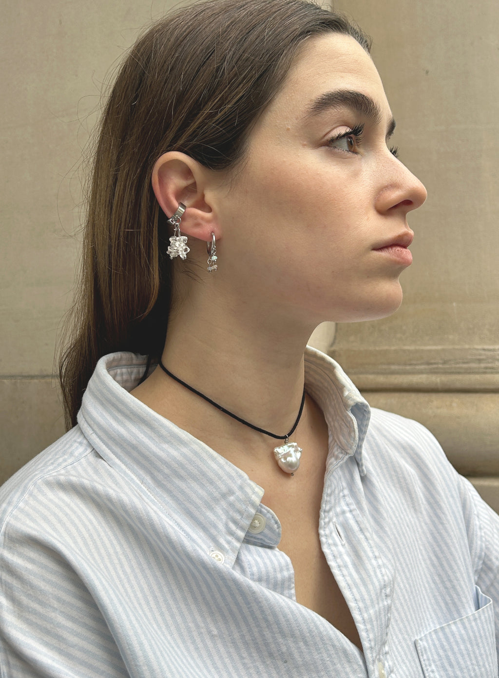 a woman in stripe blue shirt wearing a cord necklace with a baroque pearl charm with earrings with stone background 