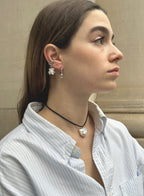 a woman in stripe blue shirt wearing a cord necklace with a baroque pearl charm with earrings with stone background 