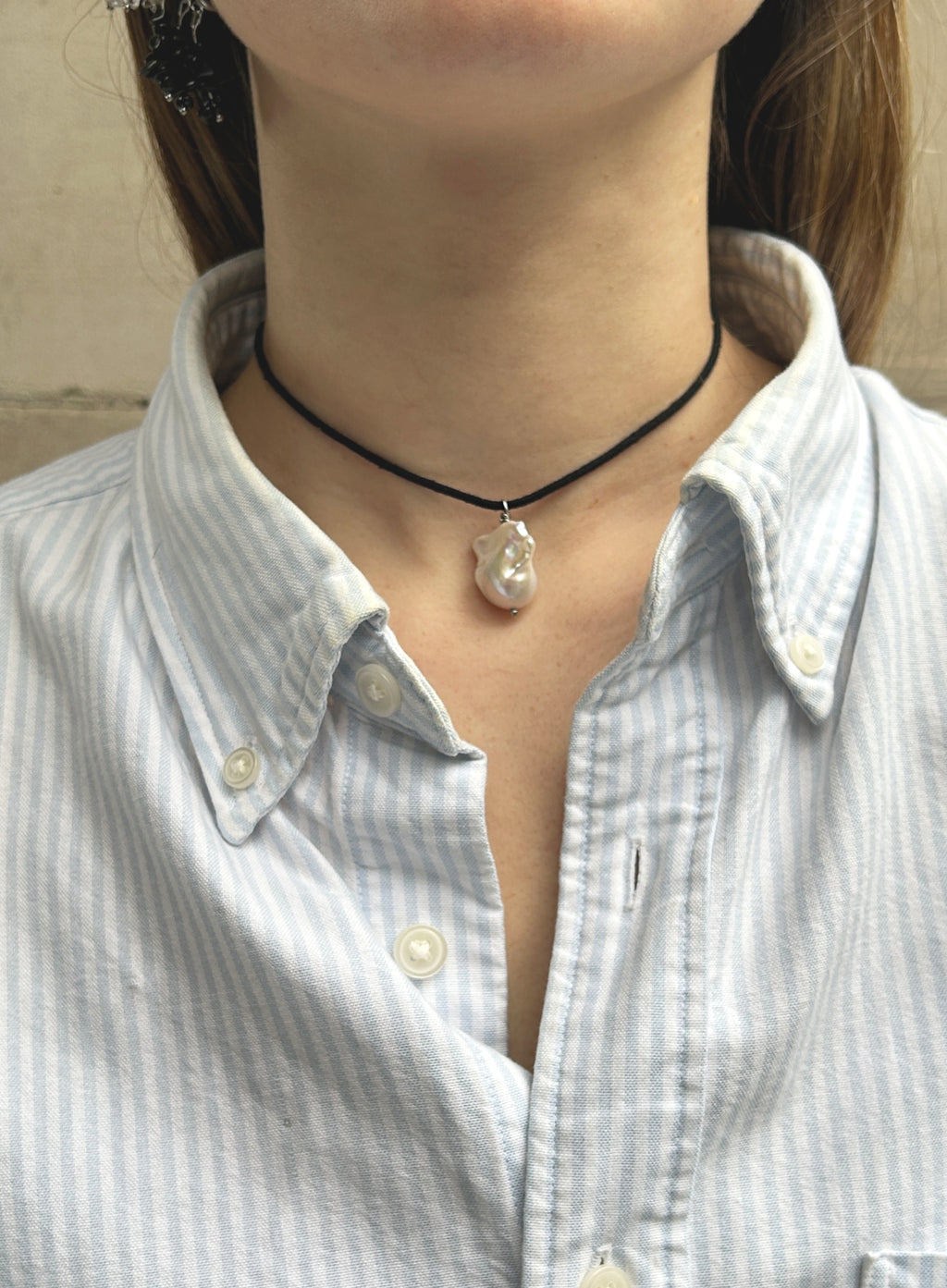 woman in stripe blue shirt wearing a cord necklace with a baroque pearl charm 