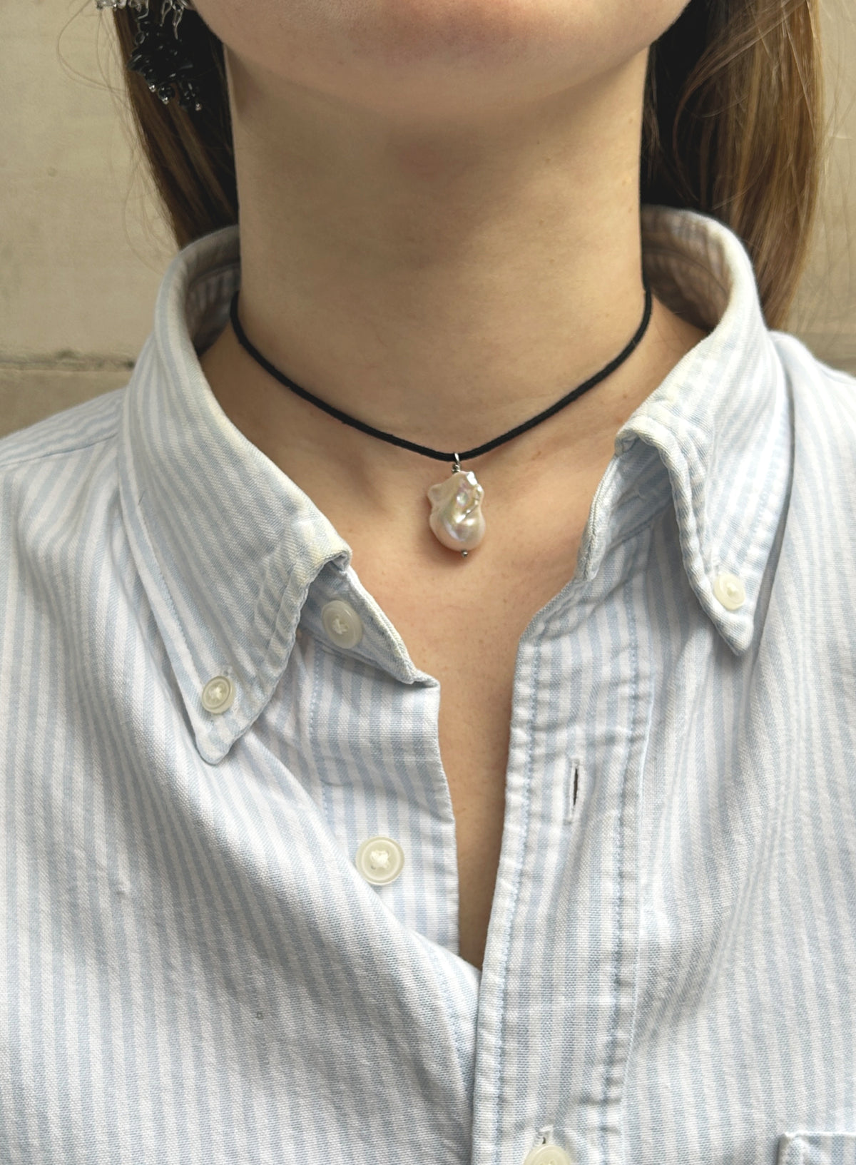 woman in stripe blue shirt wearing a cord necklace with a baroque pearl charm 