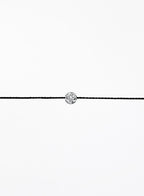 Black cord bracelet with a small round silver charm on a white background