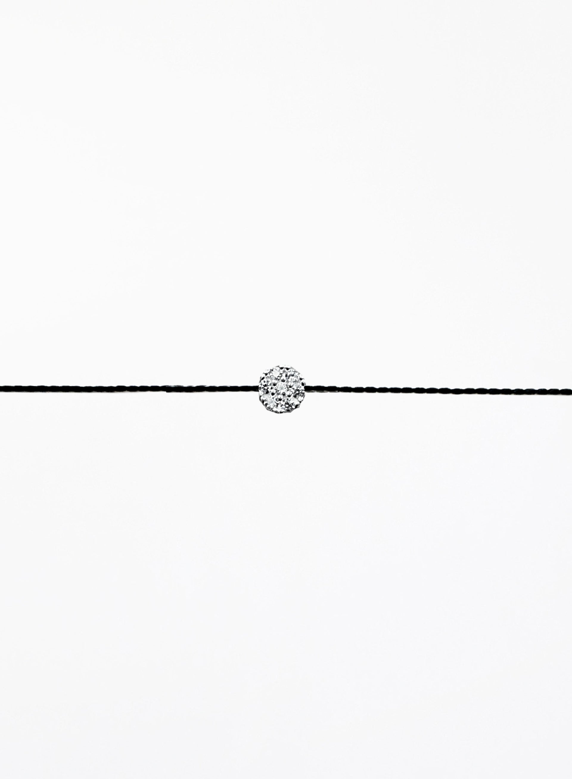 Black cord bracelet with a small round silver charm on a white background
