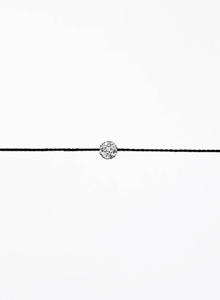 Black cord bracelet with a small round silver charm on a white background