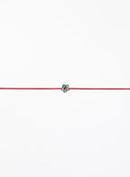 Red string bracelet with a small flower charm on a white background