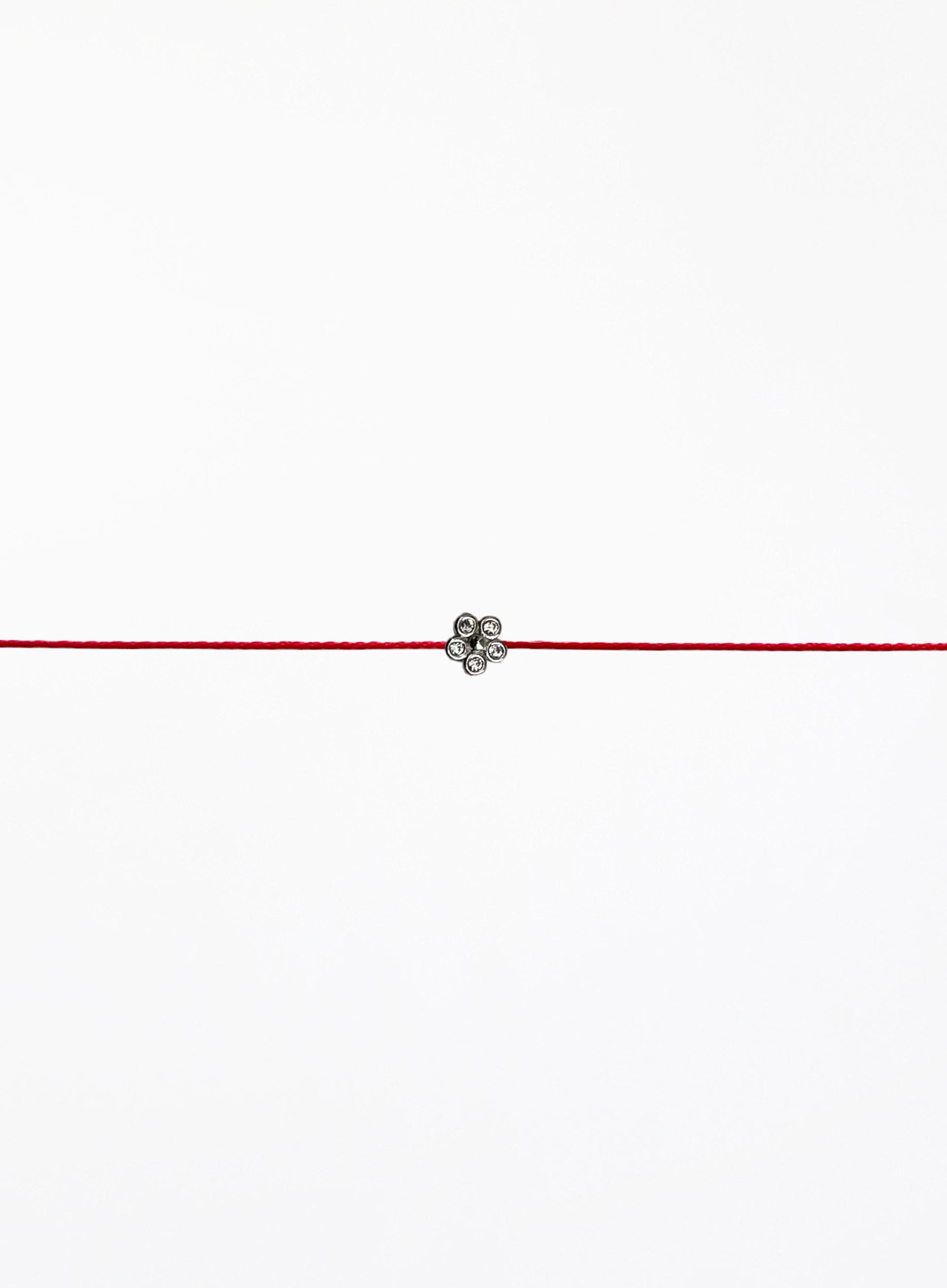 Red string bracelet with a small flower charm on a white background