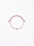 Red string bracelet with a small flower charm on a white background