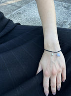 woman in black dress wearing black cord bracelet with blue stone charm and pearl charm against concrete background