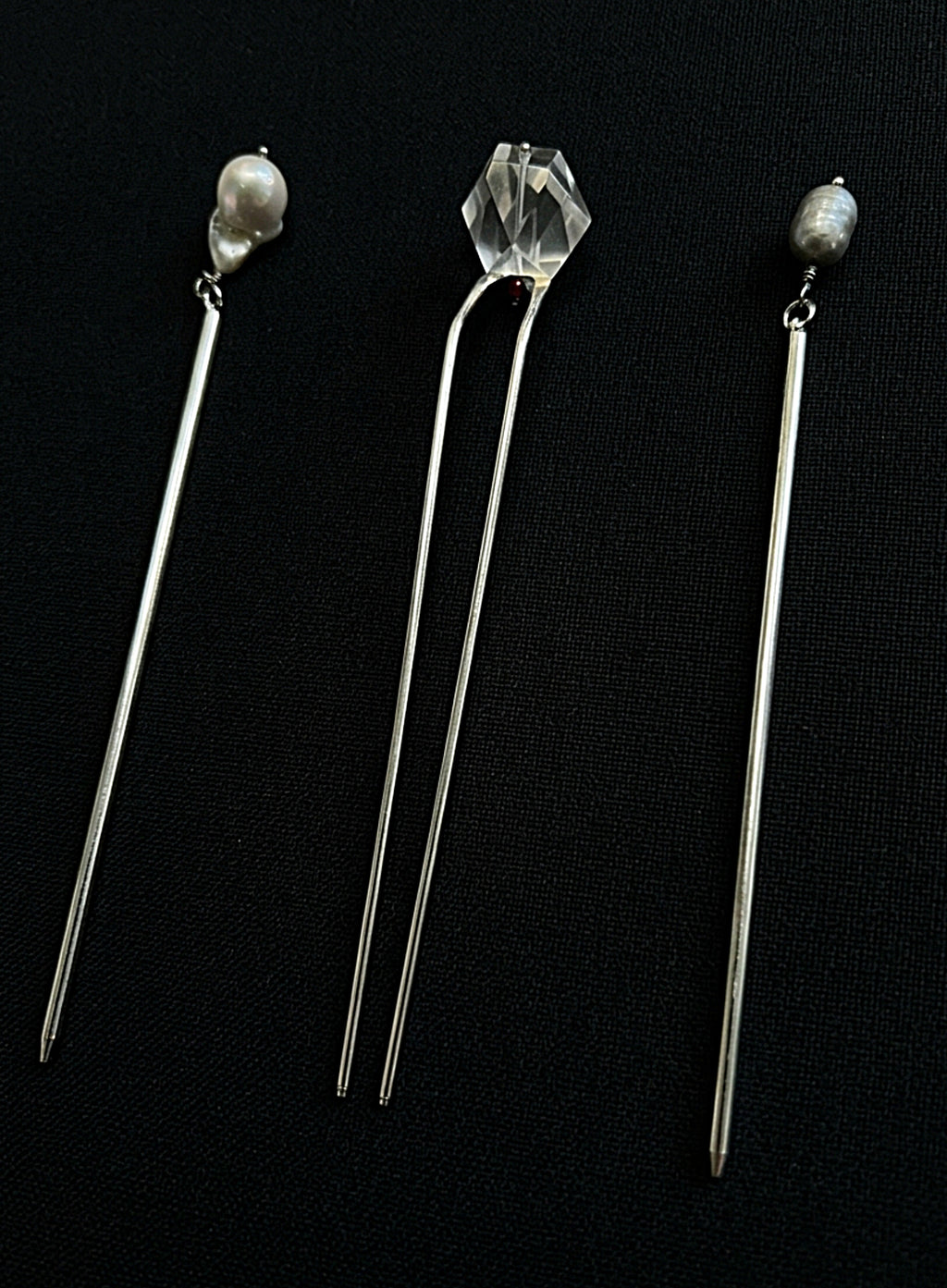 Three long silver hair pins displayed on a black background. The left and right pins feature small white pearl beads at the top, while the center pin has a faceted clear crystal bead.