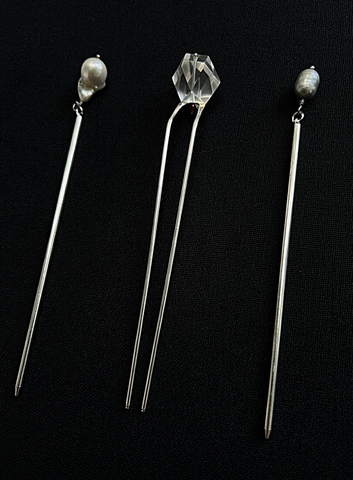 Three long silver hair pins displayed on a black background. The left and right pins feature small white pearl beads at the top, while the center pin has a faceted clear crystal bead.