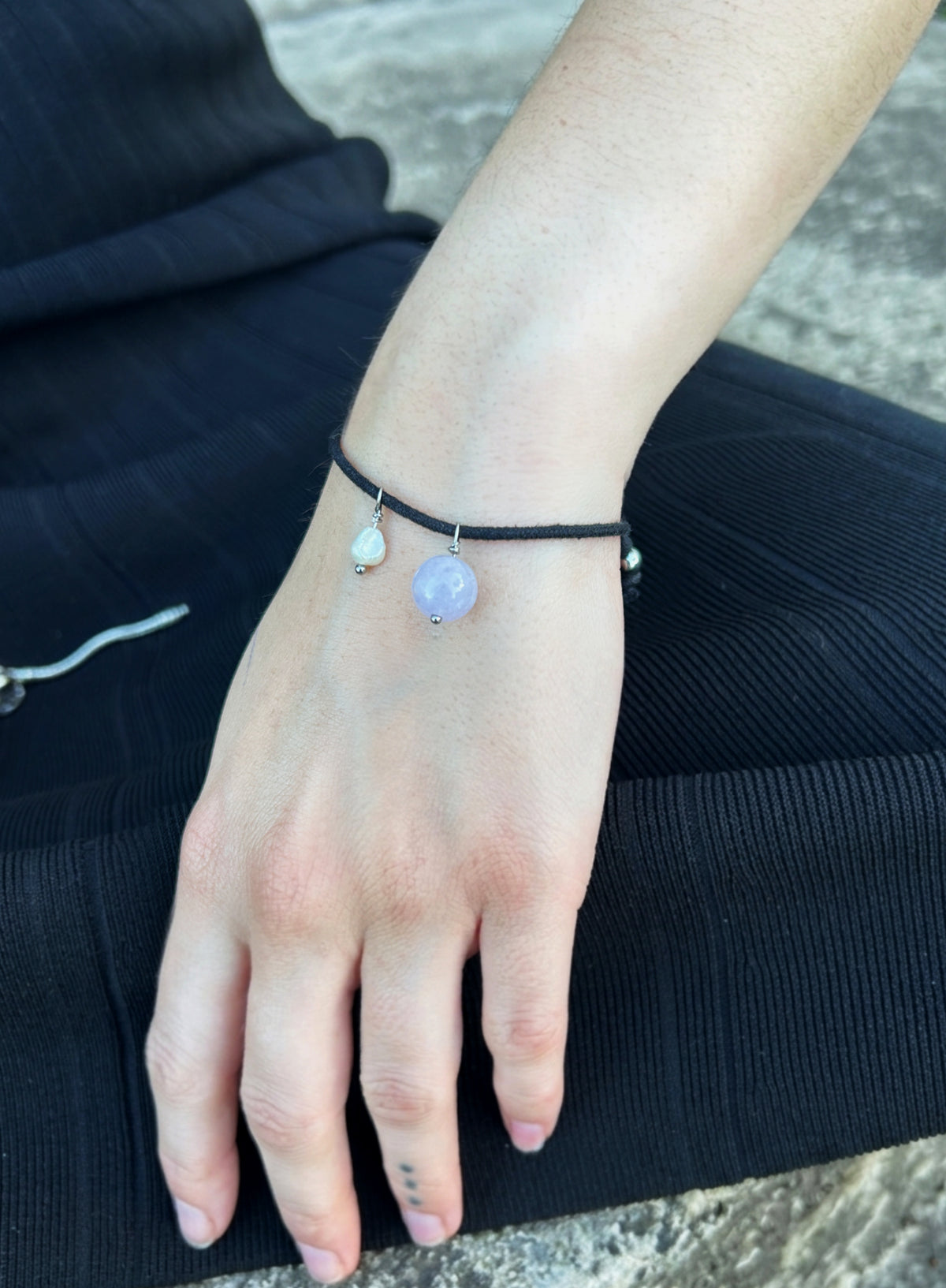 woman in black wearing a black cord bracelet with blue stone charm and pearl charm