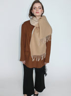Woman wearing a beige scarf with white fringe on a plain background