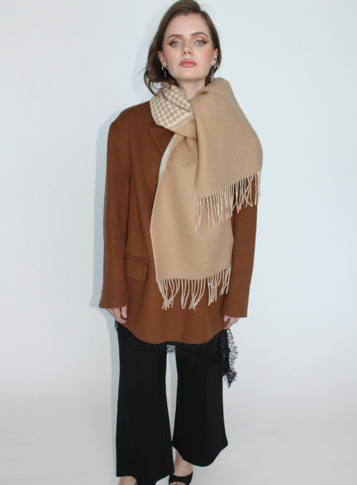 Woman wearing a beige scarf with white fringe on a plain background