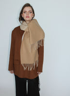 Woman wearing a beige scarf with white fringe on a plain background