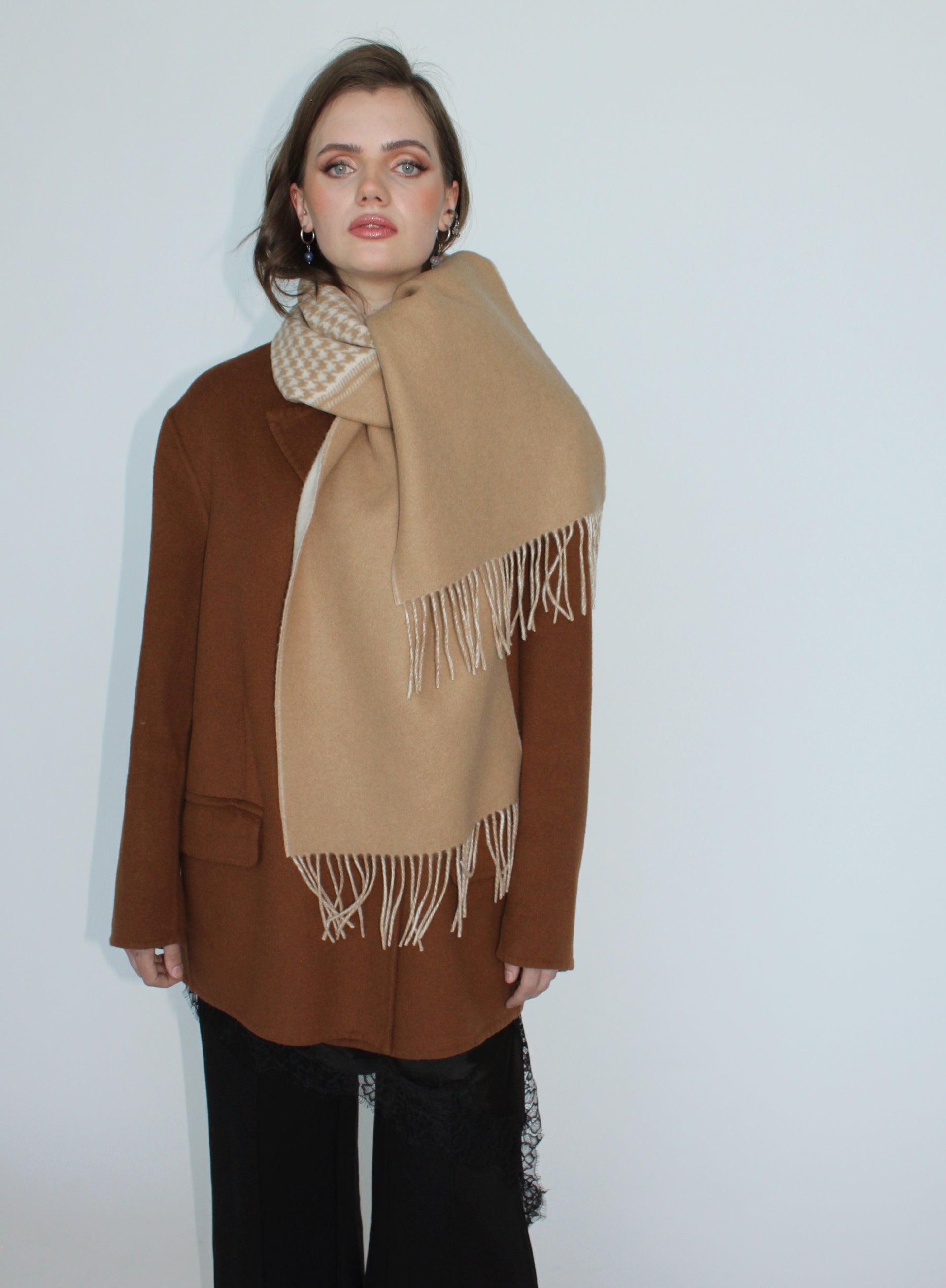 Woman wearing a beige scarf with white fringe on a plain background