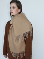 Woman wearing a beige scarf with white fringe on a plain background