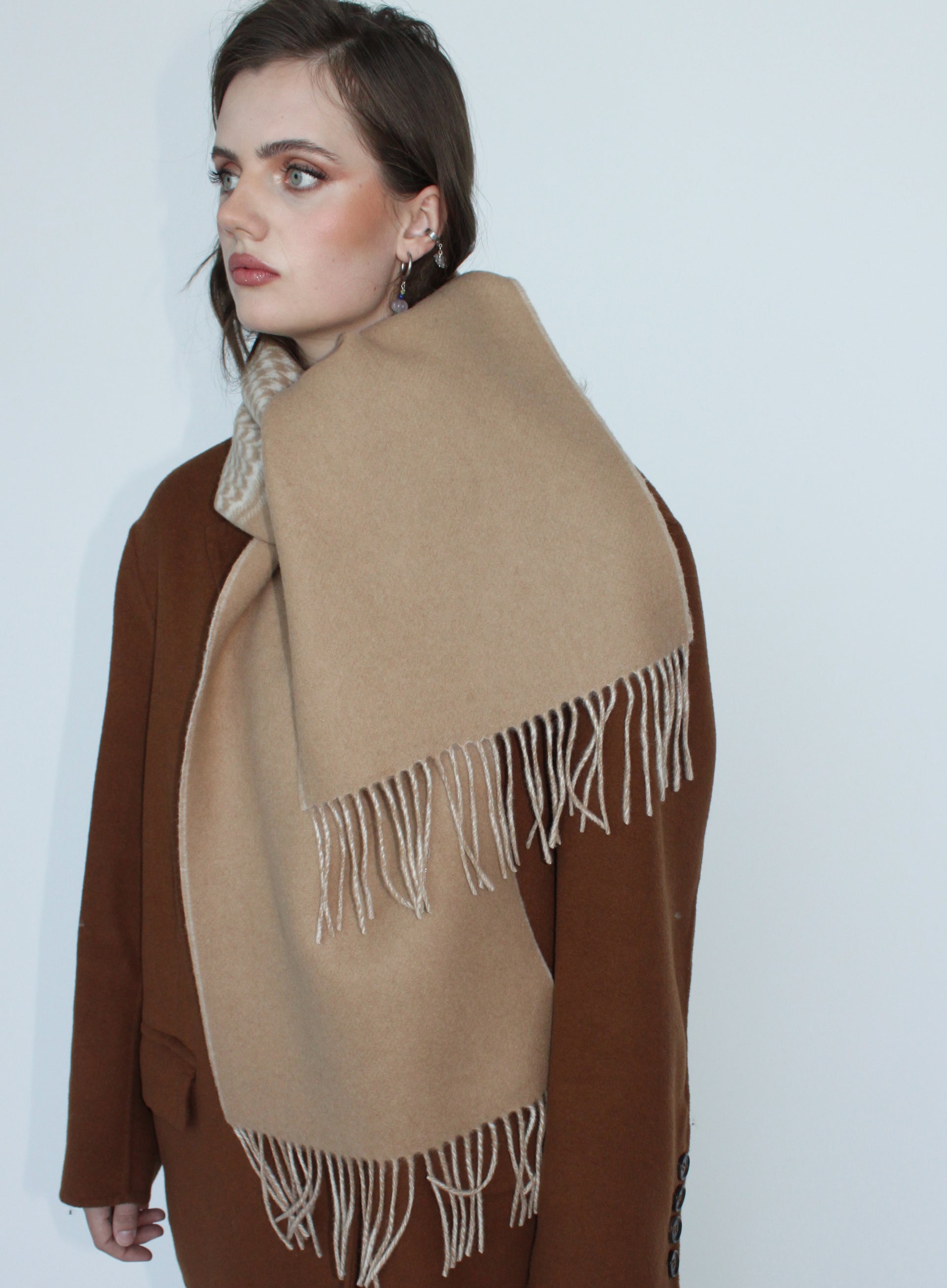 Woman wearing a beige scarf with white fringe on a plain background