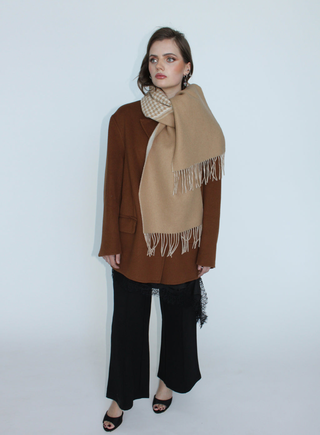 Woman wearing a beige scarf with white fringe on a plain background