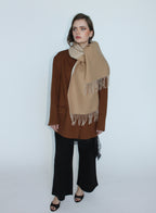 Woman wearing a beige scarf with white fringe on a plain background