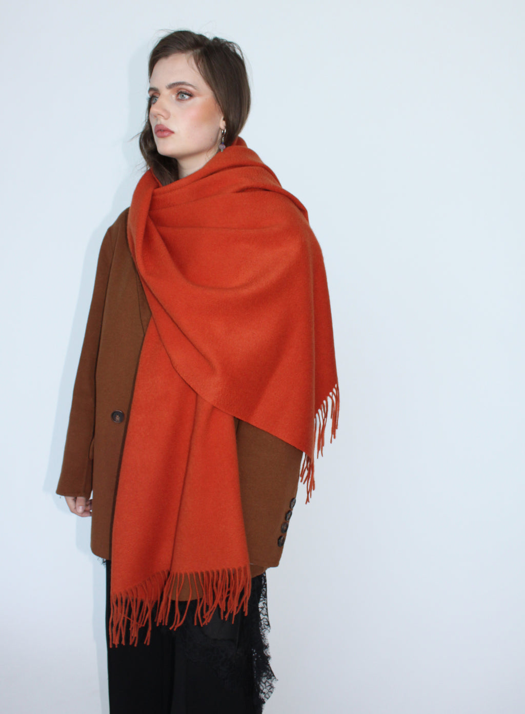 Woman wearing a large orange scarf over a brown coat on a white background