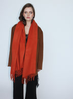 Woman wearing a large orange scarf over a brown sweater on a white background