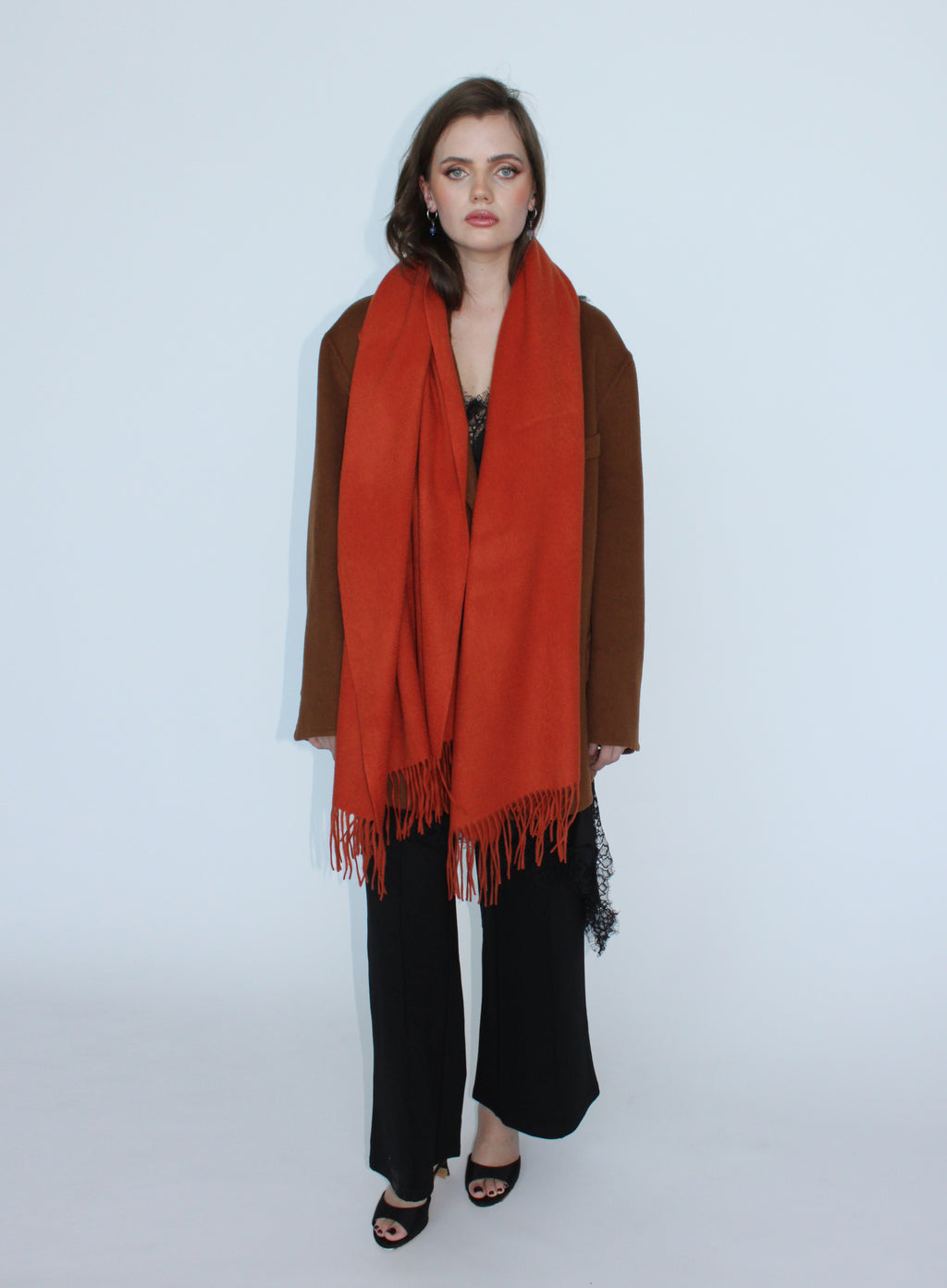 Woman wearing an orange scarf and brown coat on a white background