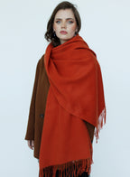 Woman wearing a large orange scarf with fringe on a white background