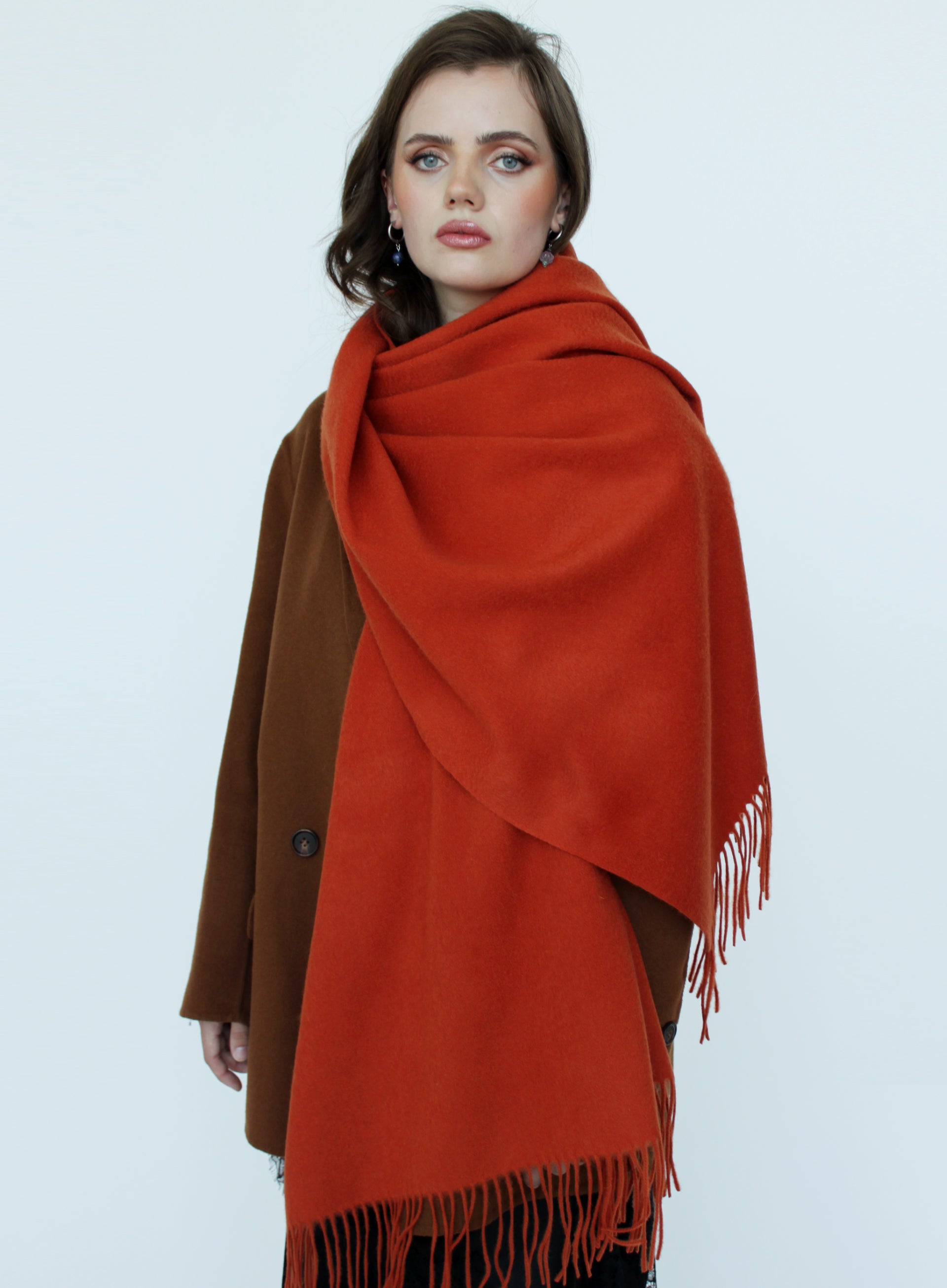 Woman wearing a large orange scarf with fringe on a white background