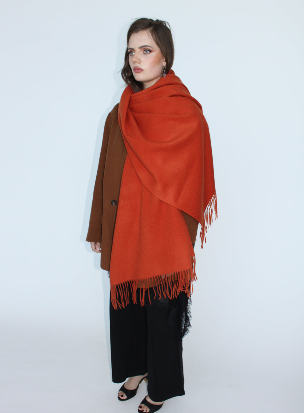 Woman wearing a large orange scarf over a brown coat on a white background