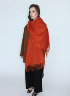 Woman wearing a large orange scarf over a brown coat on a white background