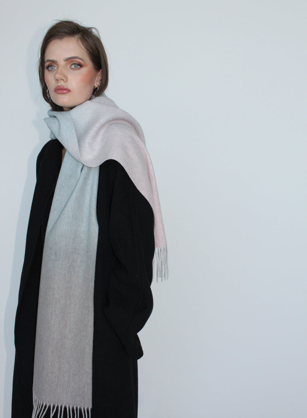 Woman wearing a light gray scarf with a black outfit against a white background