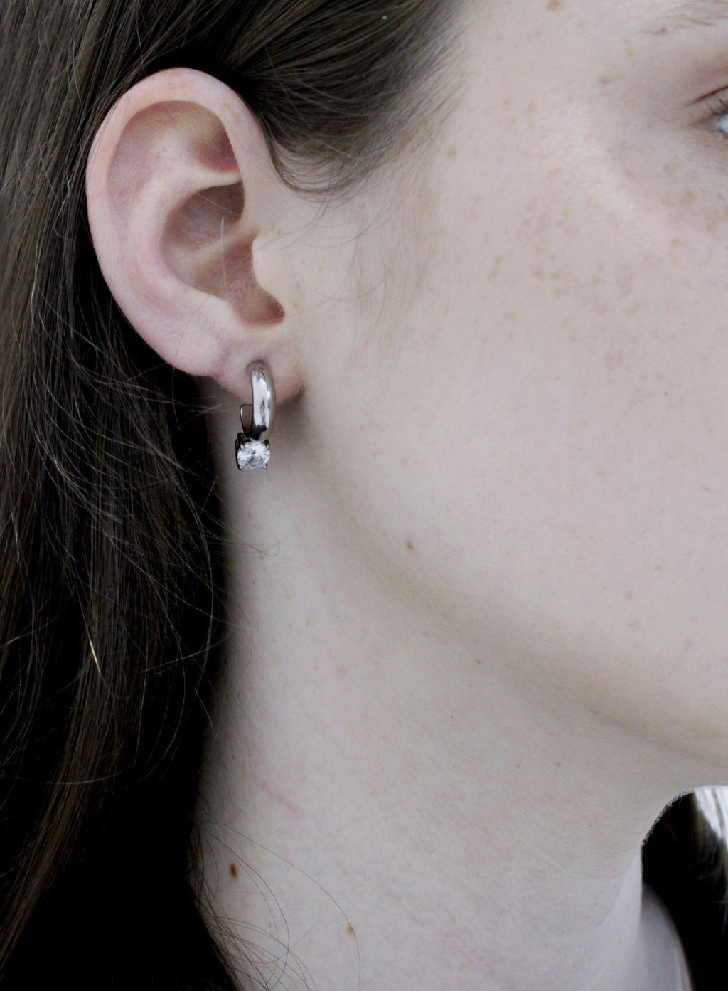 Close-up of an ear wearing a small hoop earring with a clear gemstone.