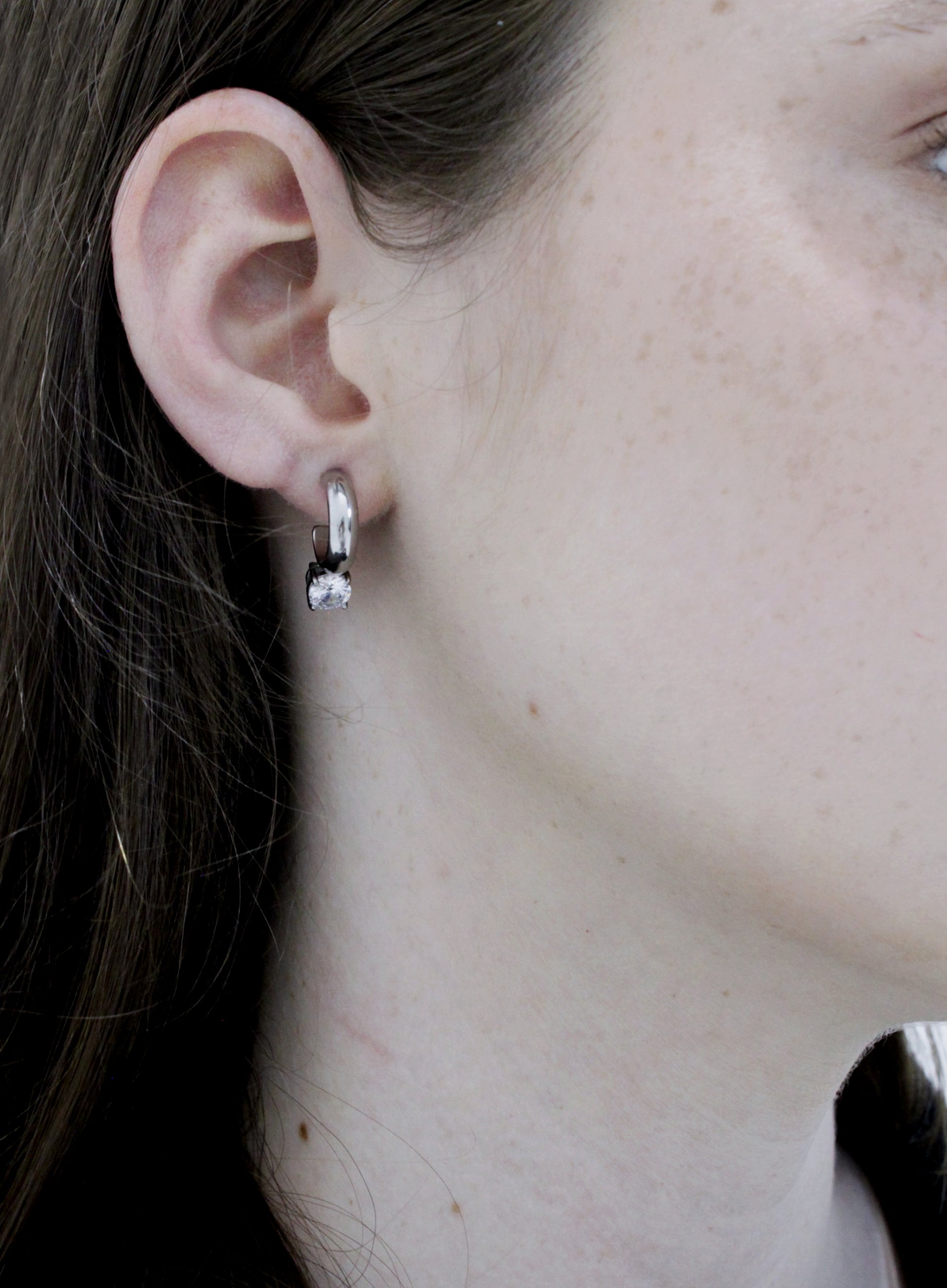Close-up of an ear wearing a small hoop earring with a clear gemstone.