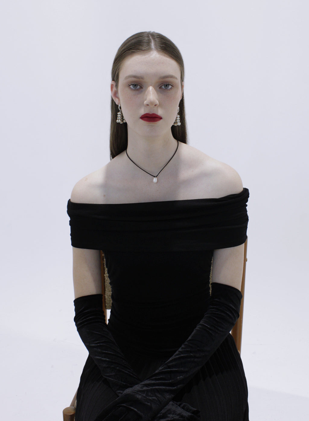 Woman wearing a black off-shoulder dress with long gloves and silver earrings with pearl chocker on a white background