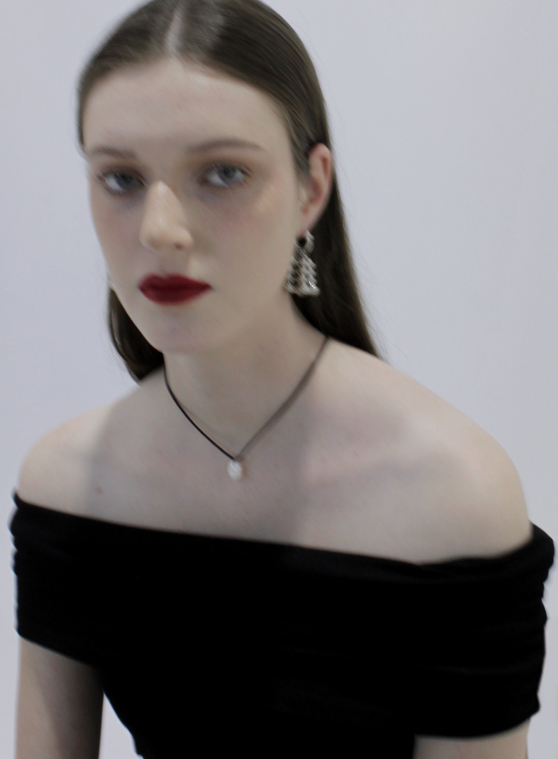 Woman wearing a black off-shoulder top with silver earrings and pearl chocker on a plain background