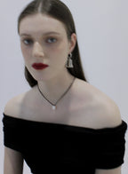Woman wearing a black off-shoulder top with pearl pendant on a plain background