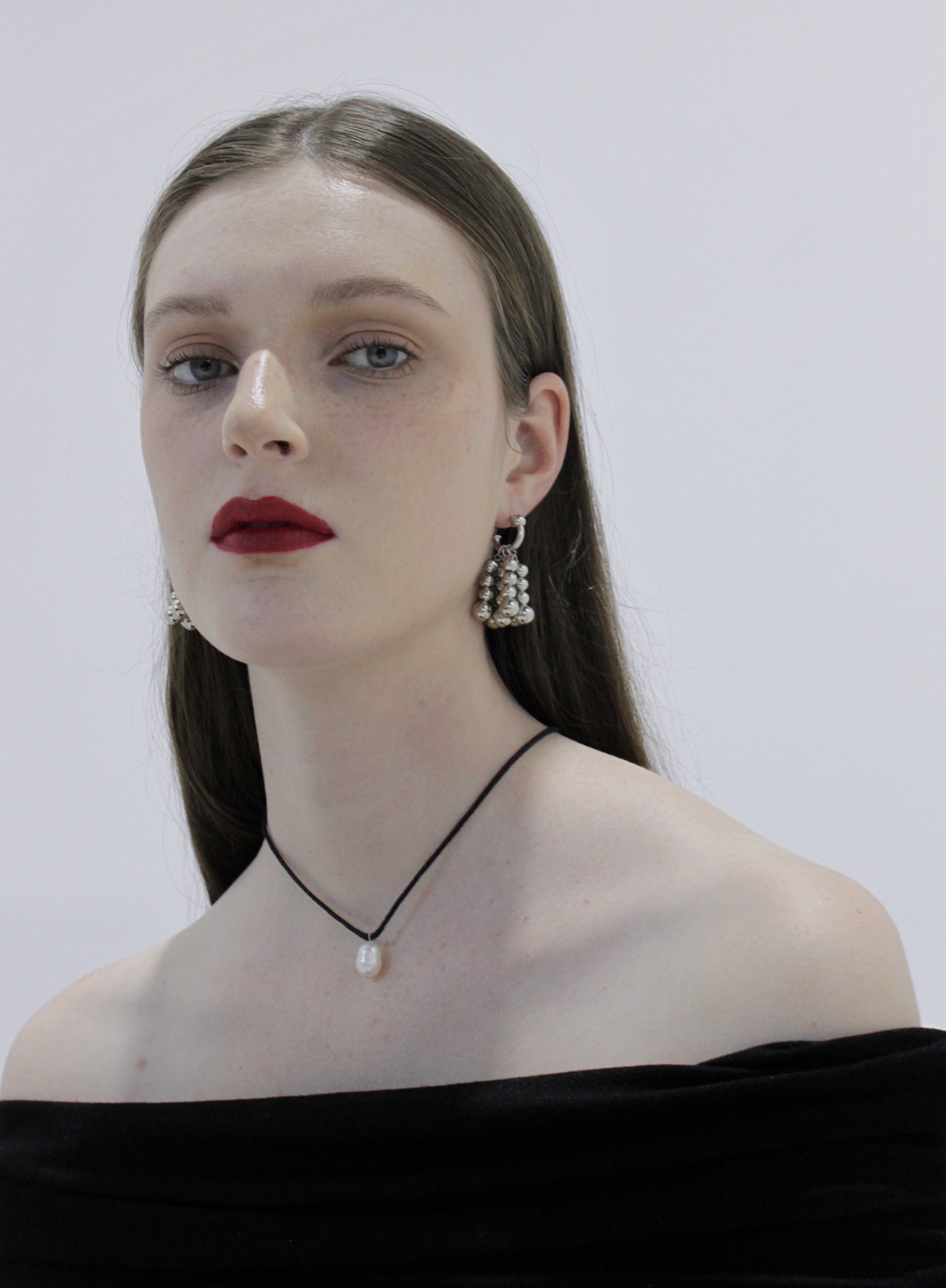 Woman wearing silver earrings and pearl necklace against a plain background