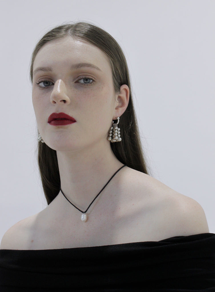Woman wearing silver earrings and pearl necklace against a plain background