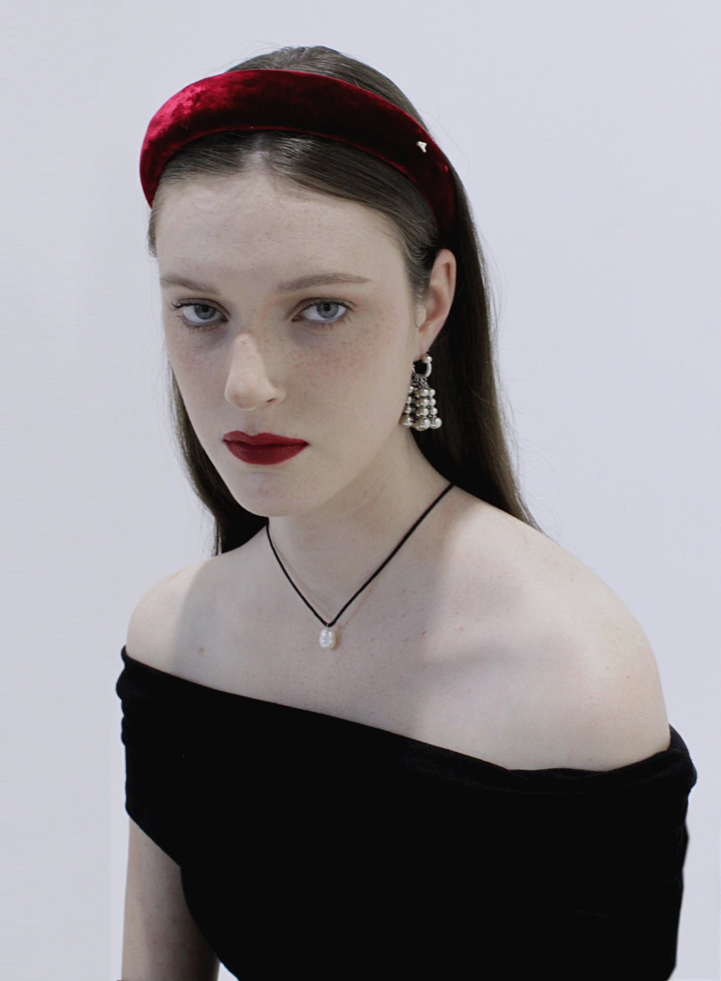 Woman wearing a red headband and black off-shoulder top against a white background