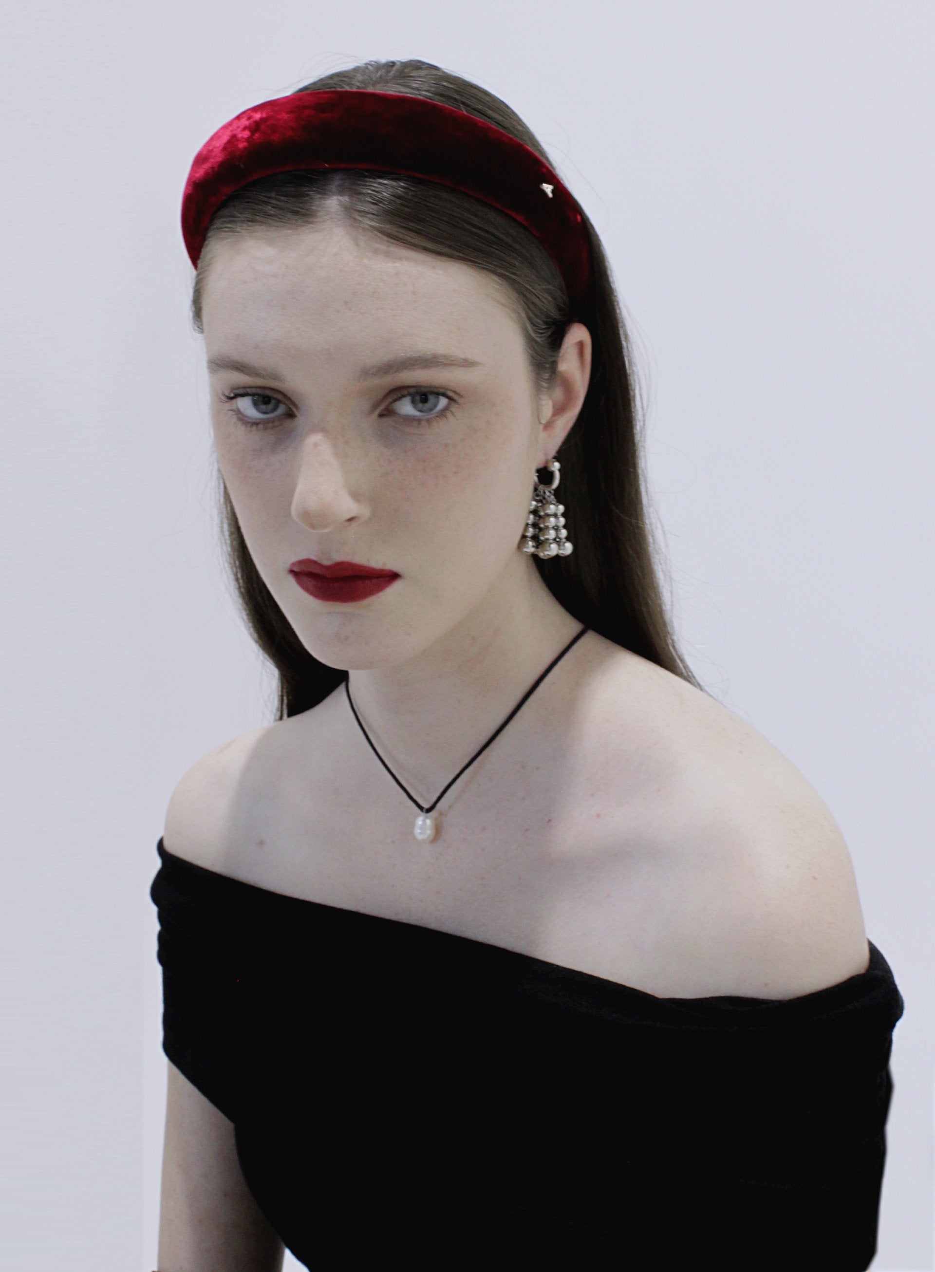 Woman wearing a red headband and black off-shoulder top against a white background