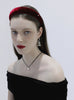 Woman wearing a red velvet headband, black off-shoulder top, and dangling earrings against a white background.