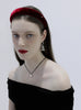Woman wearing a red velvet headband, black off-shoulder top, and dangling earrings and black chocker with pearl pendant